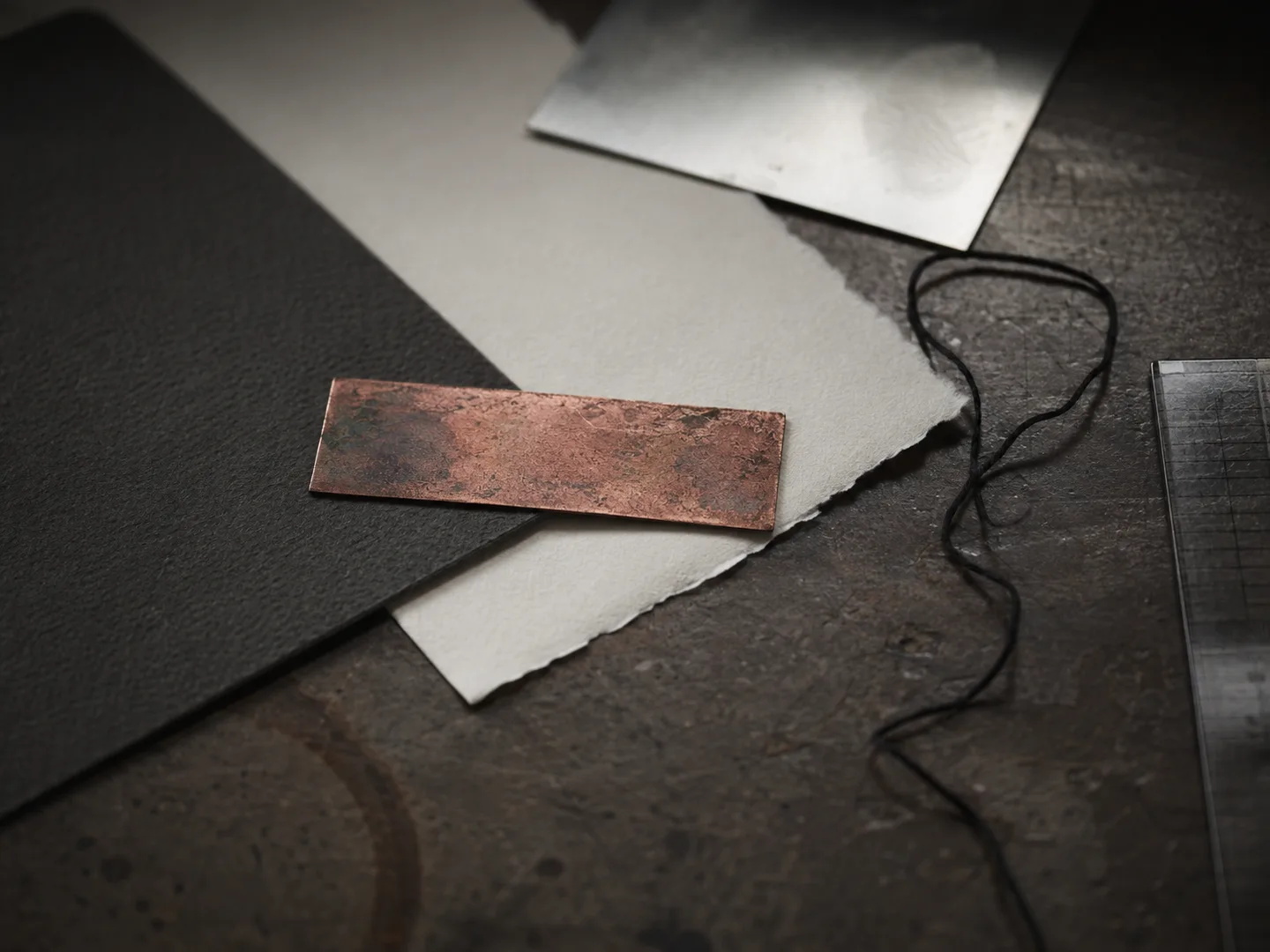 A thin copper strip laid across paper on a dark desk beside a cable.